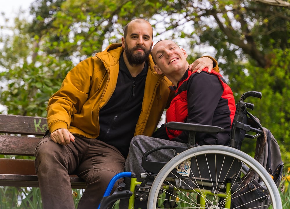 Disabled man in wheelchair sitting in the park with his father Disabled man in wheelchair sitting in the park with his father