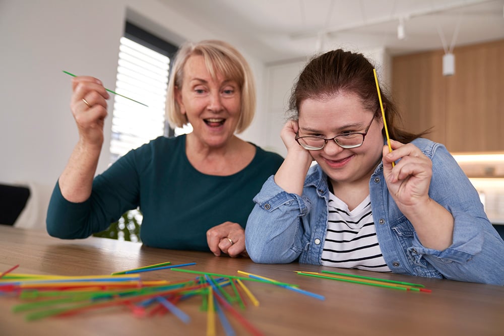 Young woman with Down Syndrome playing Pick-Up Sticks with health care aide Young woman with Down Syndrome playing Pick-Up Sticks with health care aide